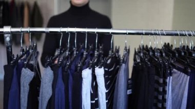 Siyah golfteki yakışıklı müşteri yeni sezon için bir çamaşırcıyı avlamaya çalışıyor. Sonbahar ve kış kıyafetleri rafların önünde duruyordu..