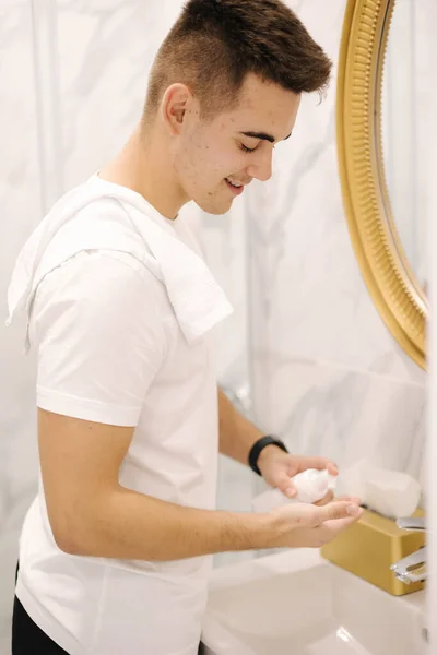 Man using cream for hands and face at home in the bathroom. Keep clean concept.