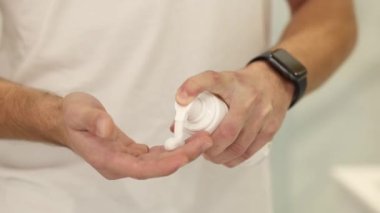 Adam banyoda tıraş köpüğü kullanıyor. Beyaz tişörtlü yakışıklı bir erkek. İlk ateş traşı. Orta seçim eller. Tıraş köpüğünü eline sürme işlemi.