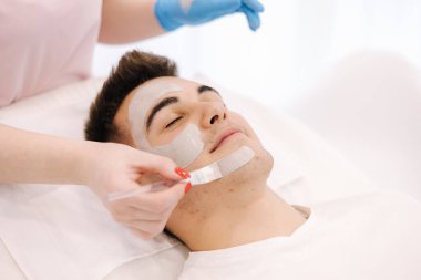 Kozmetik uzmanı spa salonundaki erkeklerin yüzüne kilden maske takıyor..