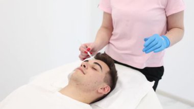 Kozmetik uzmanı spa salonundaki erkeklerin yüzüne kilden maske takıyor. Güzellik uzmanı, güzellik salonundaki yakışıklı adama dikkat ediyor..