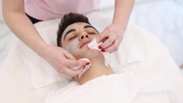 Kosmetolog Zmywa Glinianą Maskę Mokrą Serwetką Twarzy Mężczyzny Salonie Spa — Wideo stockowe