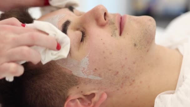 美容師は スパサロンの男性の顔から湿ったナプキンで粘土マスクを洗い流します 美容師作る美しさのためにハンサムな男で美スタジオ — ストック動画