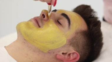Güzellik stüdyosunda altın maskeli yakışıklı bir adamın yakın çekimi. İşlem sırasında spa salonunda bir erkek. Makro. Deride sivilceler ve siyah noktalar var. Sivilce.