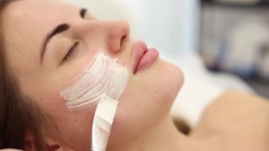 Kozmetik uzmanı spa salonundaki kadınların yüzüne kilden maske takıyor. İşlem sırasında erkek yüzünün yan görünümü
