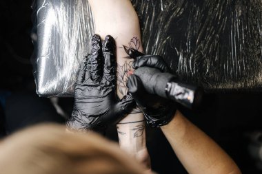 Dövme ustasının boyayla siyah dövme yapmasına yakın çekim. Usta siyah steril eldivenlerle çalışır. Genç dövme sanatçısı.
