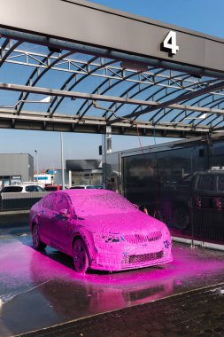 Luxury sport blue car on self servise car washing. Pink foam on auto. Close up.