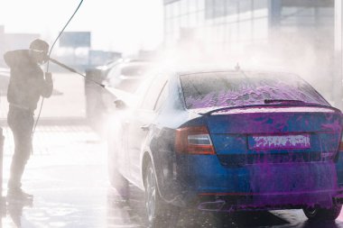 Otomobil yıkama istasyonunda arabasını yıkayan bir adam..