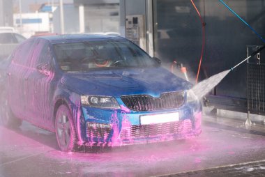 Otomobil yıkama istasyonunda arabasını yıkayan bir adam..