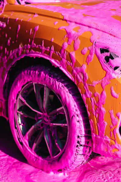 Luxury orange car on self servise car washing. Pink foam on auto.
