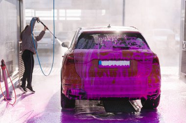 Young woman cleaning her car with a jet sprayer. Self-service car washing. Orange auto.