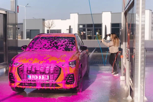 Young woman cleaning her car with a jet sprayer. Self-service car washing. Orange auto.