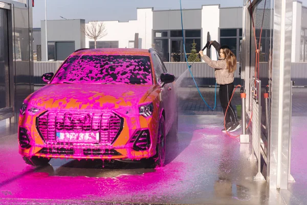Young woman cleaning her car with a jet sprayer. Self-service car washing. Orange auto.
