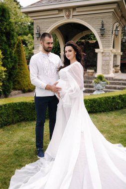 Elegant pregnant woman in luxury white dress walking aroung with her handsome husband.