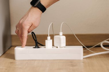 Human hand puts the charger into a filled extension cord. White cable connector. High quality photo