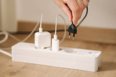 Human hand puts the charger into a filled extension cord. White cable connector. High quality photo