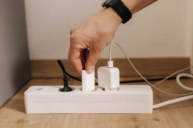 Human hand puts the charger into a filled extension cord. White cable connector. High quality photo