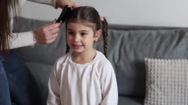 A mother makes her daughters hair, combs her hair and weaves braids. Four year girl is preparing for kindergarten. High quality 4k footage