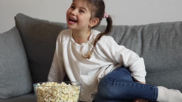 可爱的小女孩坐在沙发上 在家看电视 可爱的女孩吃爆米花 假日气氛 高质量的照片 — 图库视频影像