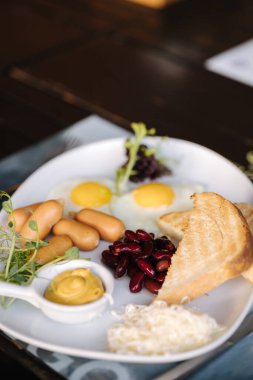 English breakfast. Fried eggs, red beans, mini sausages, butter, mustard and toasted bread. High quality photo