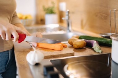 Close-up of female hand using knife and cutting carrot on wooden table. Home food concept . High quality photo