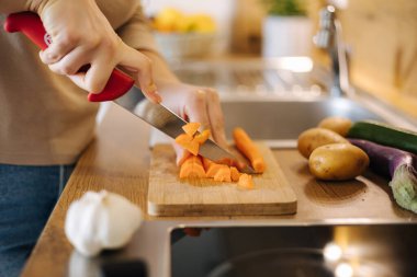 Close-up of female hand using knife and cutting carrot on wooden table. Home food concept . High quality photo