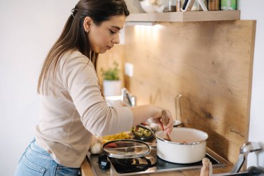 Sebzeleri tencerede hazırlayan kadının yan görüntüsü. Kadın ahşap kaşıkla malzemeleri karıştırıyor. Yüksek kalite fotoğraf