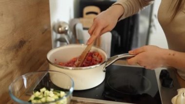 Ahşap kaşık kullanan ve beyaz tenceredeki malzemeleri karıştıran bir kadın. Yüksek kalite 4k görüntü