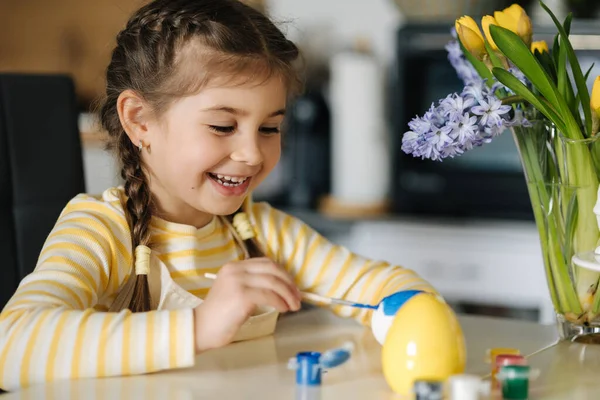 可爱的4岁女孩穿着米黄色围裙坐在厨房桌子上 画着复活节彩蛋 高质量的照片 — 图库照片