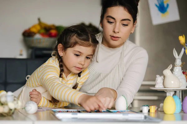 妈妈和她可爱的小女孩坐在厨房的桌子边 用铅笔给照片涂色 高质量的照片 — 图库照片