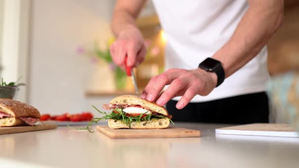 Красивый Молодой Человек Режет Итальянский Сэндвич Показывает Внутри Вкусный Обед — стоковое видео