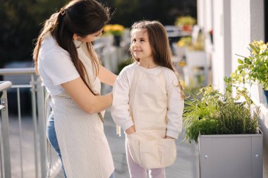 Güzel genç anne kızının balkonda bahçe işleri için giyinmesine yardım ediyor. Yüksek kalite fotoğraf