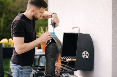 Adam mangal yapmak için bir paket kömür açıyor. Arka bahçede barbeküye hazırlanıyorum. Yüksek kalite fotoğraf