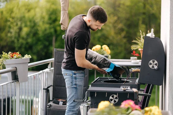 stock image Man pours out charcoal into BBQ grill on terrace. Male preparing for backyard barbecue . High quality photo