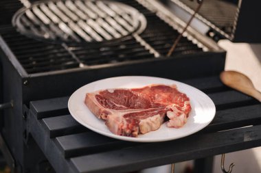 Barbekü ızgarasının yanındaki beyaz tabakta çiğ biftek. Taze kalite biftek. Yüksek kalite fotoğraf