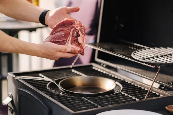 İnsan eli ızgaranın önünde T-Bone Bifteği tutuyor. Mangal konsepti. Yakın plan. Yüksek kalite fotoğraf