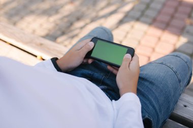 Genç çocuk okuldan sonra parkta akıllı telefonuyla online oyunlar oynuyor..