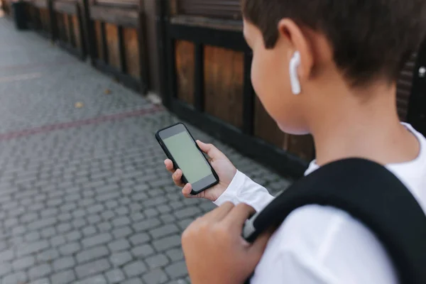 ワイヤレスヘッドフォンを備えた10代の少年のモックアップは 携帯電話を使用しています 緑の画面 — ストック写真