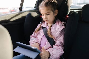 Tatlı küçük kız anaokuluna giderken araba koltuğunda tablet kullanıyormuş. Yüksek kalite fotoğraf