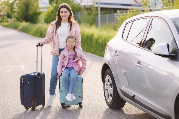 stock image Family standing by the car with suitcases and waiting journey. Mom and daughter preparing for trip. Little girl sitting on kid suitcase. . High quality photo