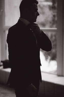 Şık damadın silueti büyük pencerenin önünde duruyor. Damat sabahı. Yüksek kalite fotoğraf