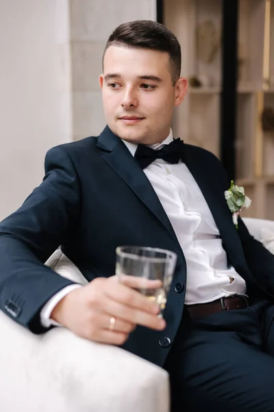 Snygg Brudgum Mörkblå Kostym Sitter Stol Med Glas Whisky Brudgumsmorgonen — Stockfoto