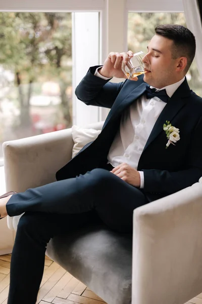 Przystojny Pan Młody Ciemnoniebieskim Garniturze Siedzący Krześle Szklanką Whisky Panny — Zdjęcie stockowe