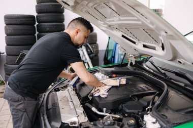 Garajında çalışan erkek bir tamircinin portresi. Genç sakallı adam arabanın motorunu kontrol ediyor, kaput açık. Yüksek kalite fotoğraf