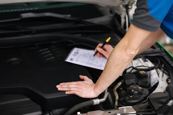 stock image Closeup of a man writing on a clipboard in a garage on open hood. High quality photo