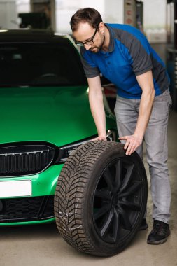 Adamın biri arabadan tekerlek yuvarlıyor. Araba servisinde tekerlek değiştirmek. Yüksek kalite fotoğraf