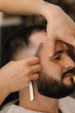 Traş olurken keskin bıçak kullanan berberin yan görüntüsü. Berber dükkanında oturan yakışıklı müşteri. Yüksek kalite fotoğraf