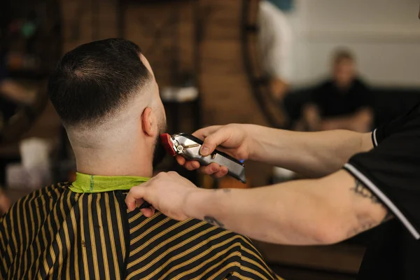 Professional barber shaves mans hairs in barber shop. Back view of customer . High quality photo