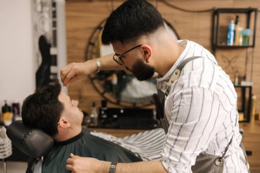 Berber dükkanında iplik kullanma prosedürü. Profesyonel berber, kaş şeklini düzeltiyor. Sandalyede oturan erkek müşteri. Yüksek kalite fotoğraf