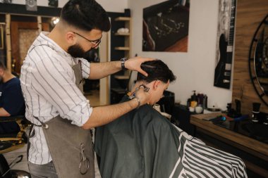 Berber dükkanında kendine güvenen erkek müşterinin saçını kesen yakışıklı sakallı adam. Yüksek kalite fotoğraf